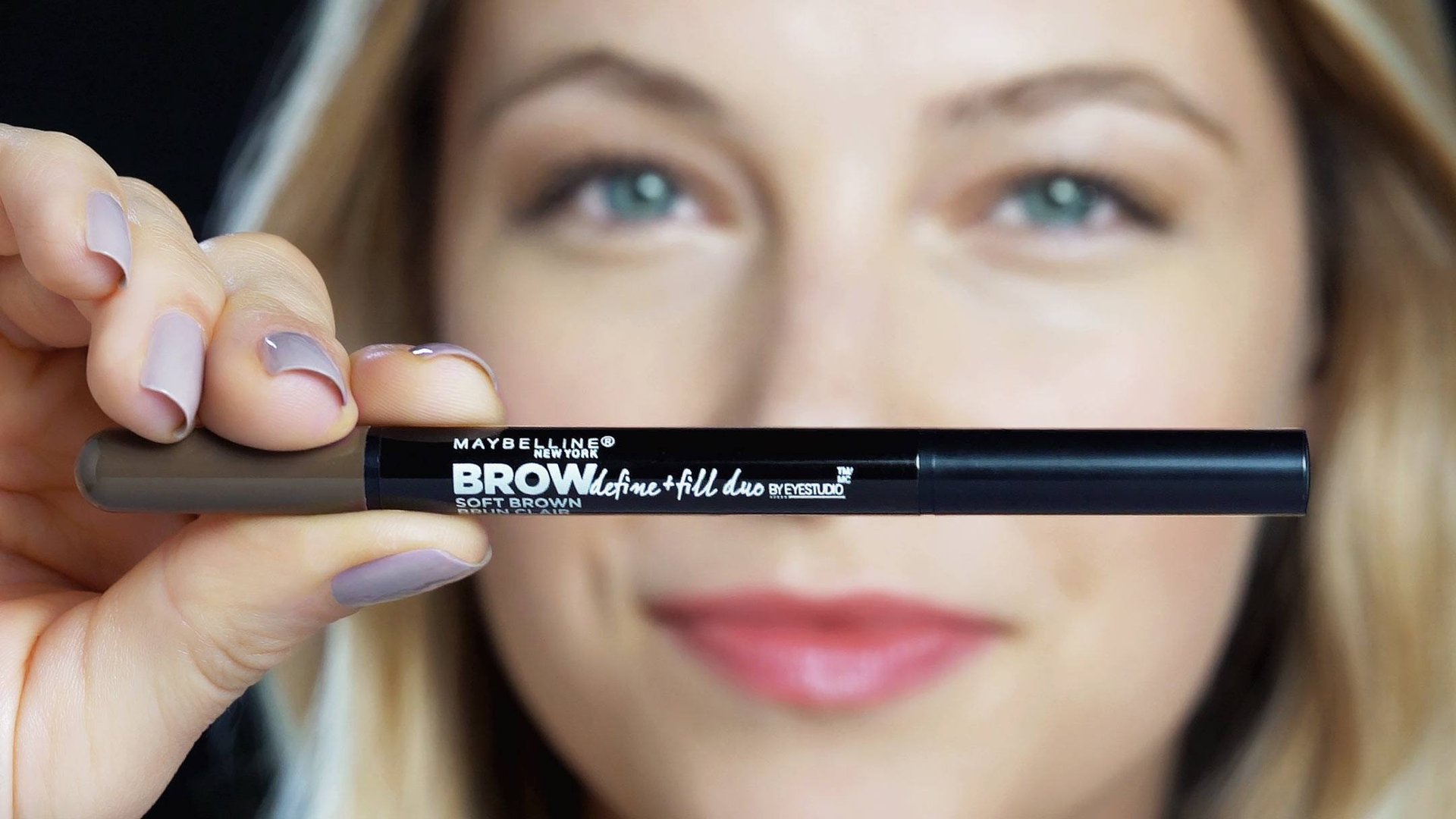 Fokus på et Maybelline Brow Define and Fill duoprodukt, holdt av en blond kvinne 